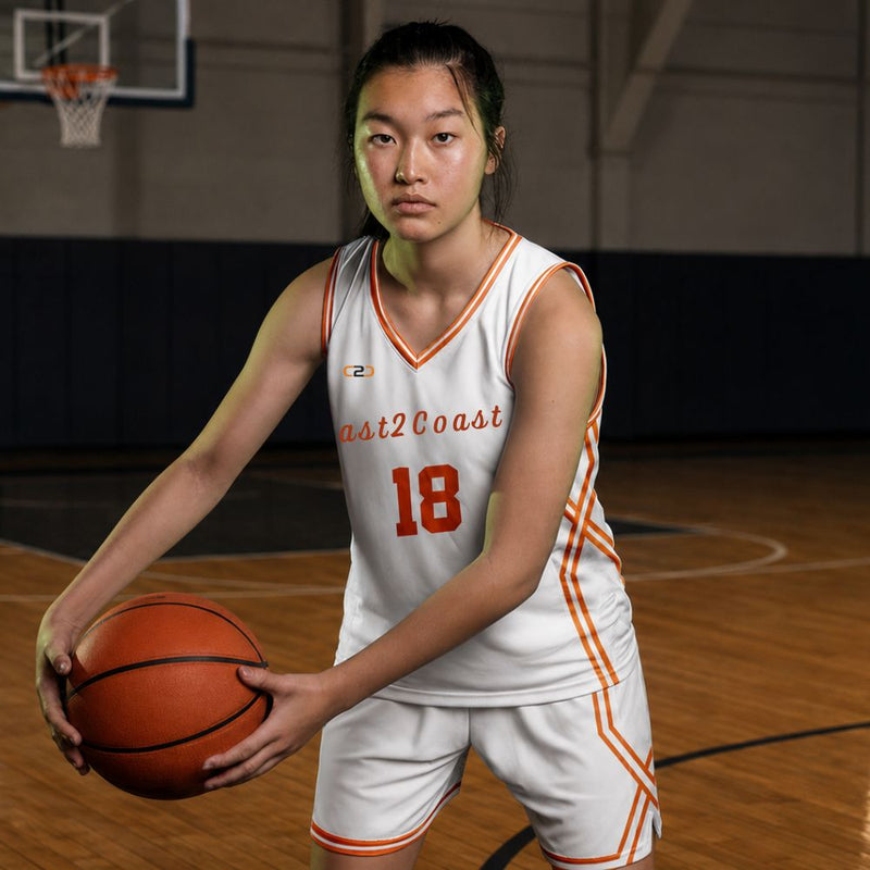 Female player holding a basketball in a white Coast2Coast uniform on an indoor court